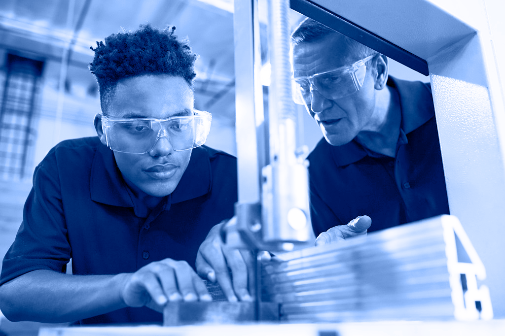 Student working with a bandsaw while supervised by an instructor