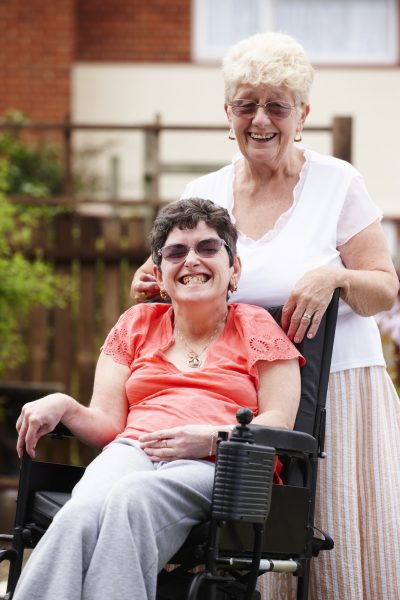 A disabled woman smiling in a wheelchair accompanied by a caretaker, an older woman