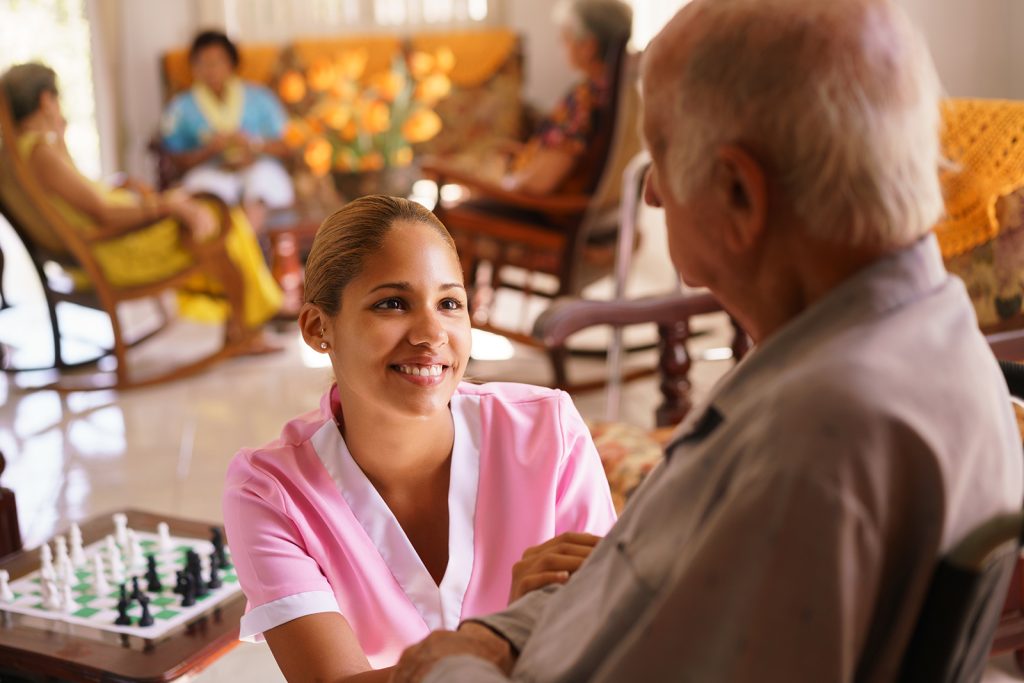 A smiling nurse looks up at a man in an assisted living facility 