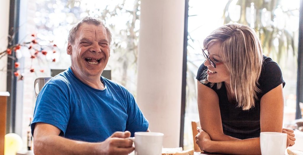 A man with disabilities and woman laughing and having coffee