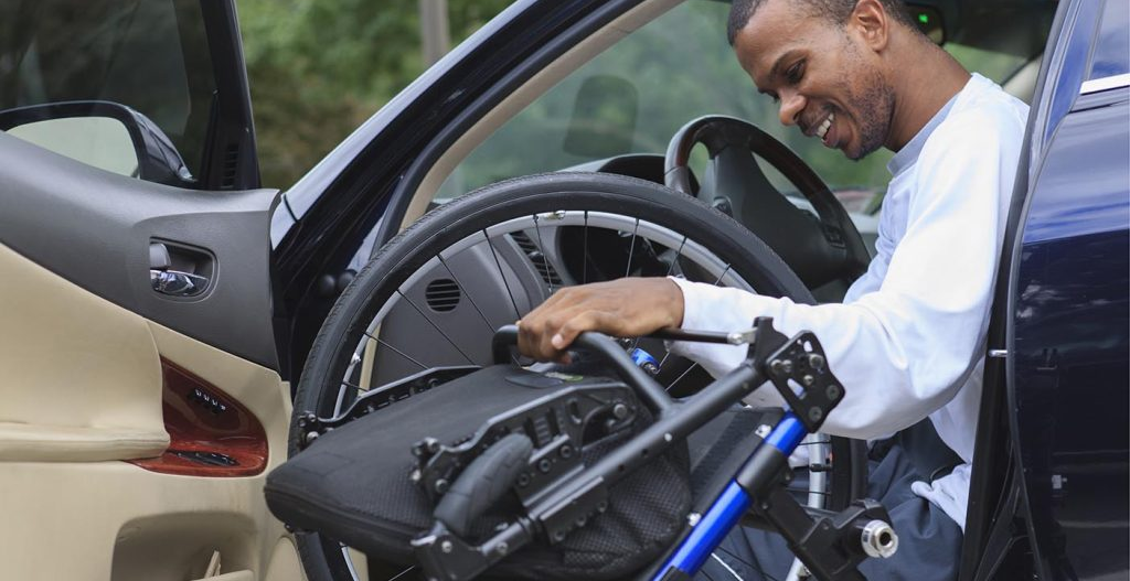 Man sitting in drivers seat of a car putting away his wheelchair