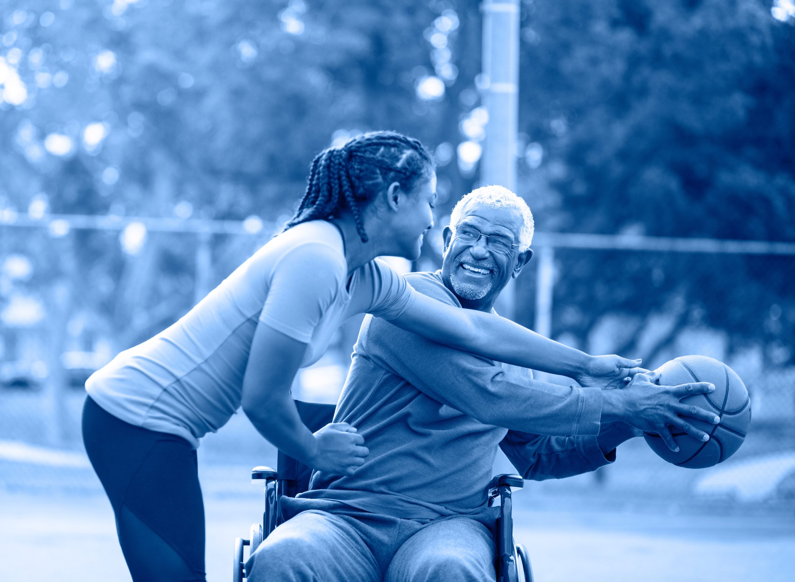 Girl playing basketball with her grandfather who is in a wheelchair. Both are laughing.