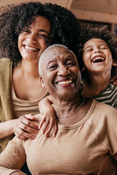 Black elderly woman smiling and being hugged by her laughing family, a daughter and grandchild