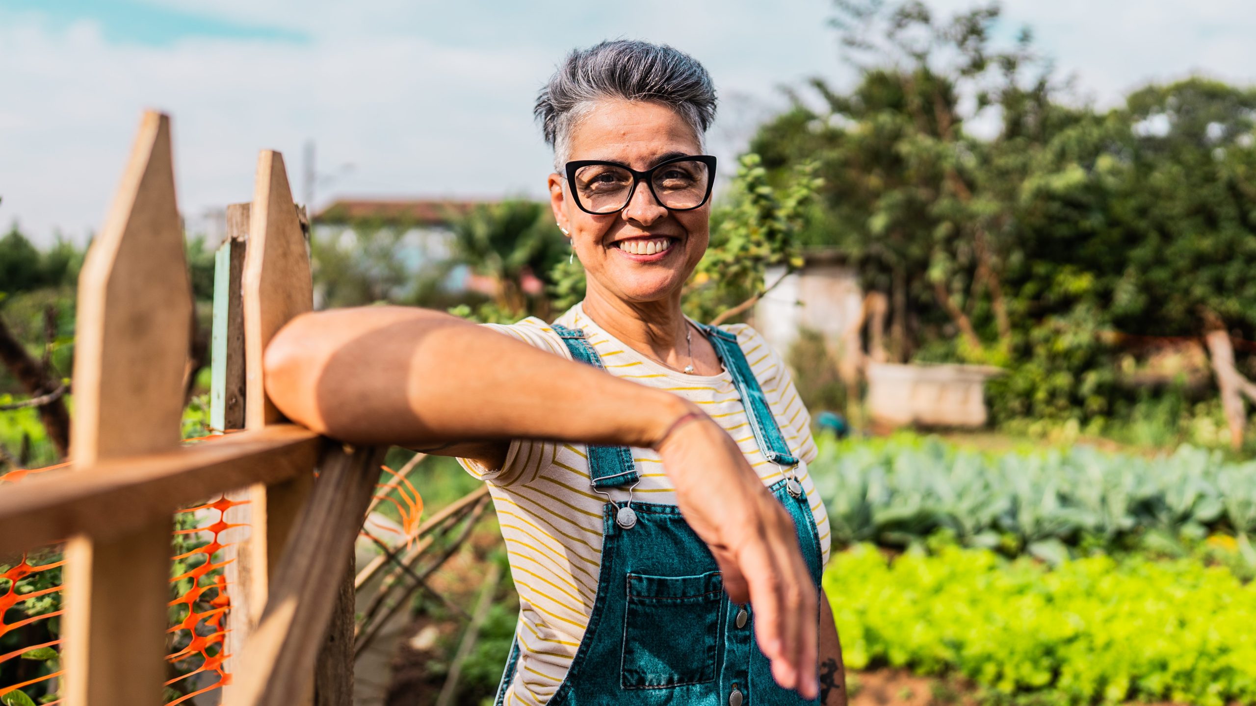 A farming woman stands by a fence in her garden
