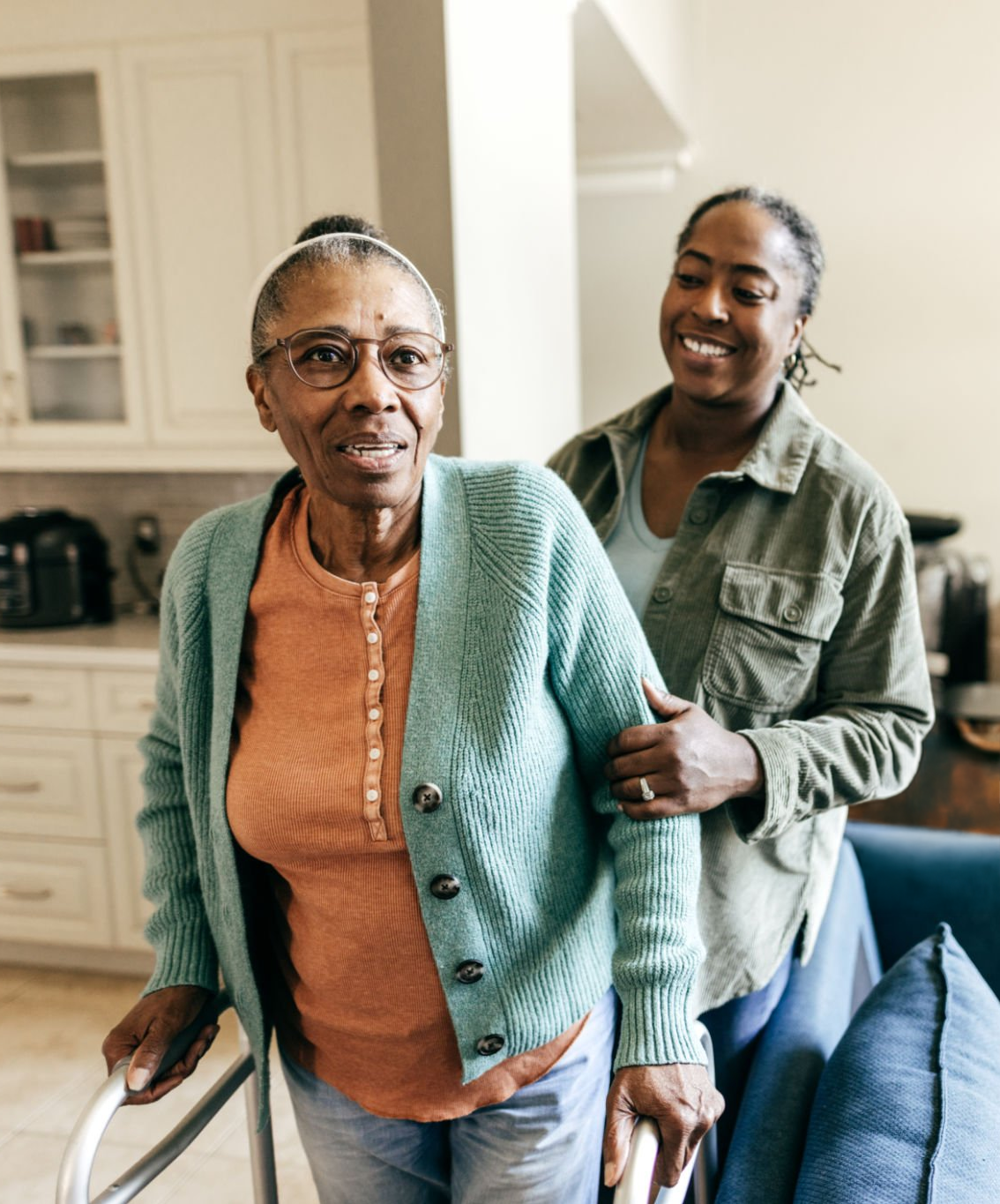 An elderly woman using a walker is assisted by a family member holding onto her arm